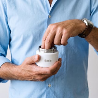 Hands holding an open Basis bottle against a blue shirt